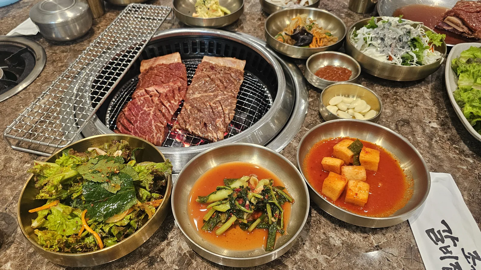 Overhead view of charcoal-grilled galbi in progress with full spread of Korean BBQ side dishes at Jogane Galbi