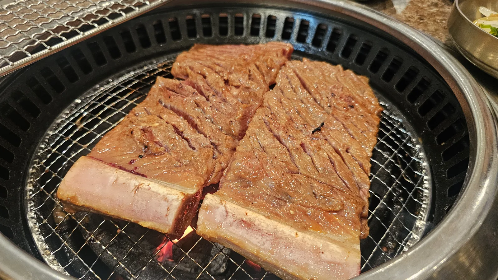 Bone-in beef galbi mid-cook on charcoal grill showing browned exterior forming at Jogane Galbi Mokdong