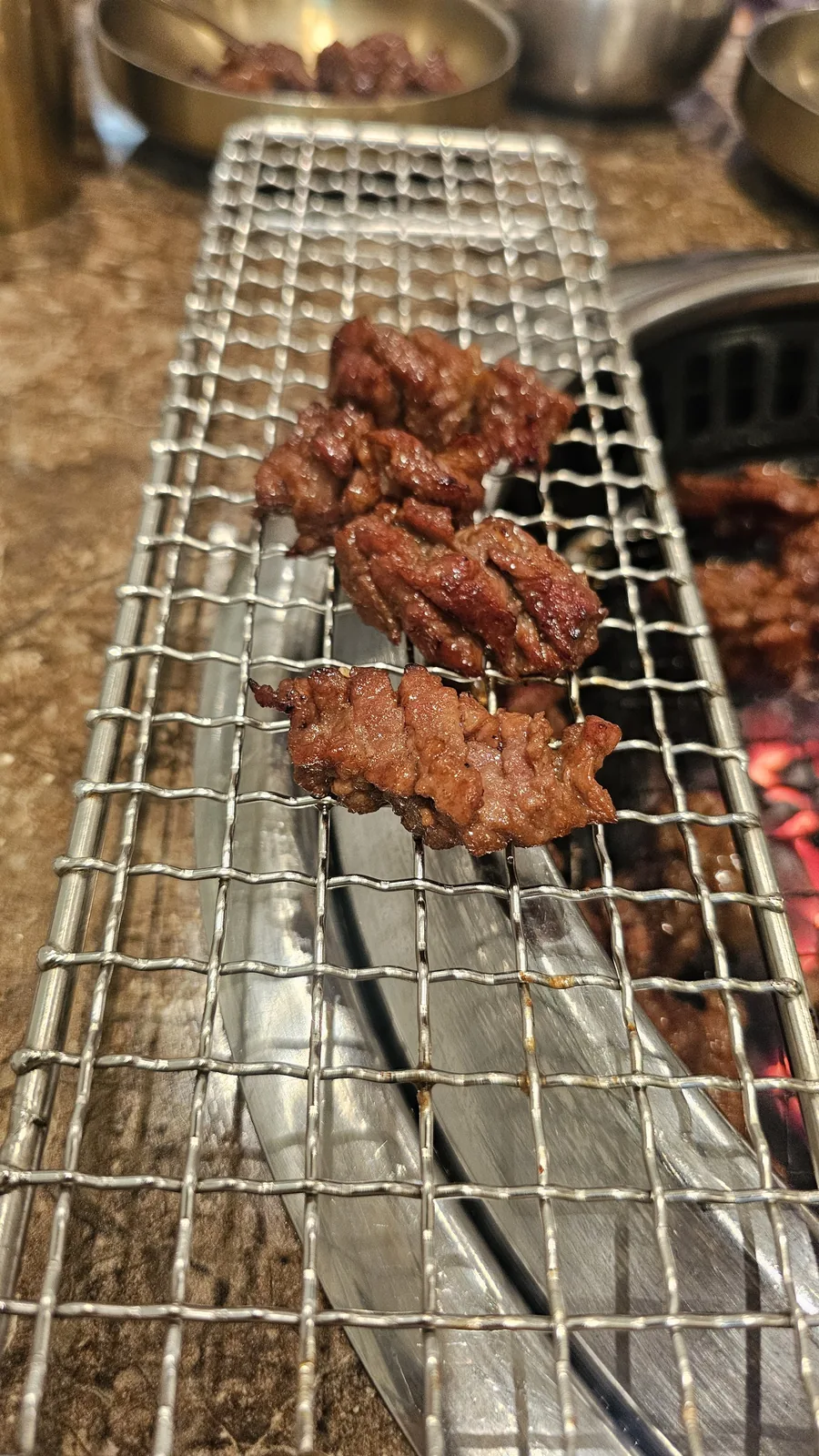 Grilled galbi pieces resting on secondary warming rack above charcoal heat at Jogane Galbi