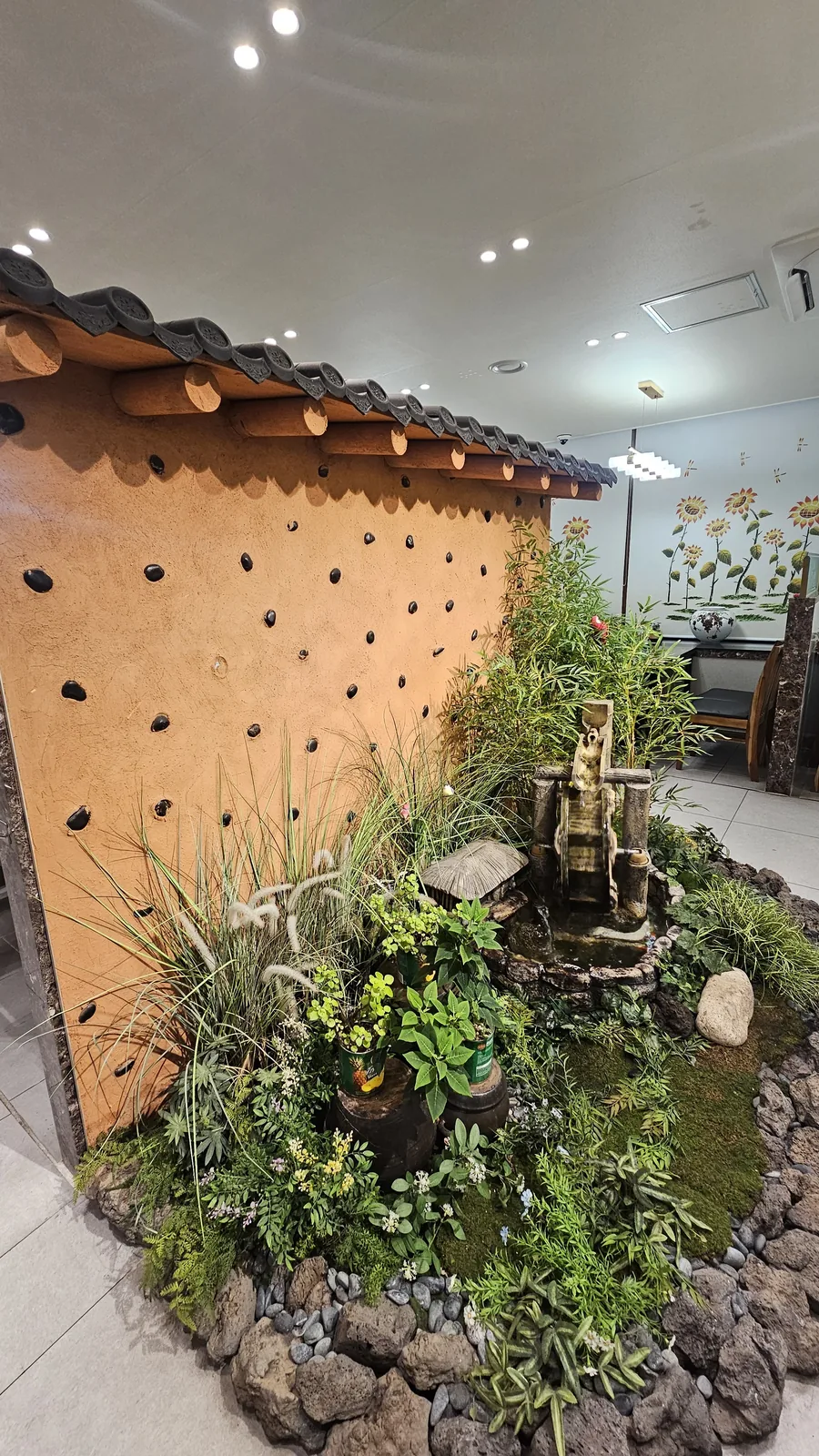 Traditional Korean hanok-style interior of Jogane Galbi — clay walls, curved tile roofline, garden sculptures, and water wheel