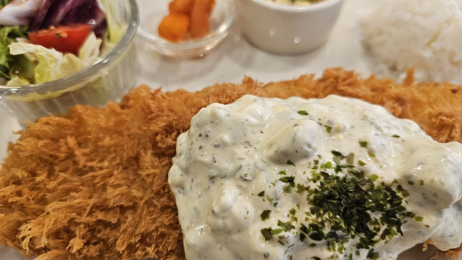 Close-up of golden crispy pork donkatsu with creamy tartare sauce and herb garnish at Keebo