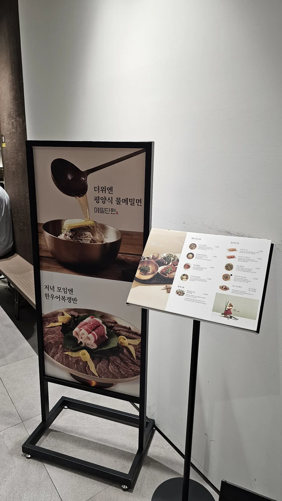 Promotional standup sign at Meomil Danpyeon entrance featuring cold buckwheat noodles menu