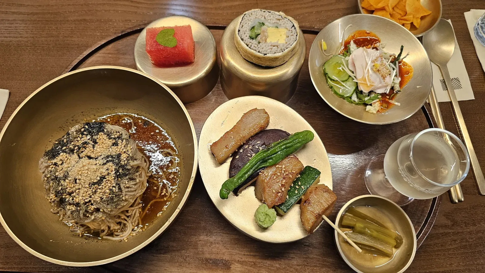 Meomil Danpyeon bansang tray with perilla oil buckwheat noodles topped with sesame seeds and seaweed flakes, watermelon dessert, and side dishes