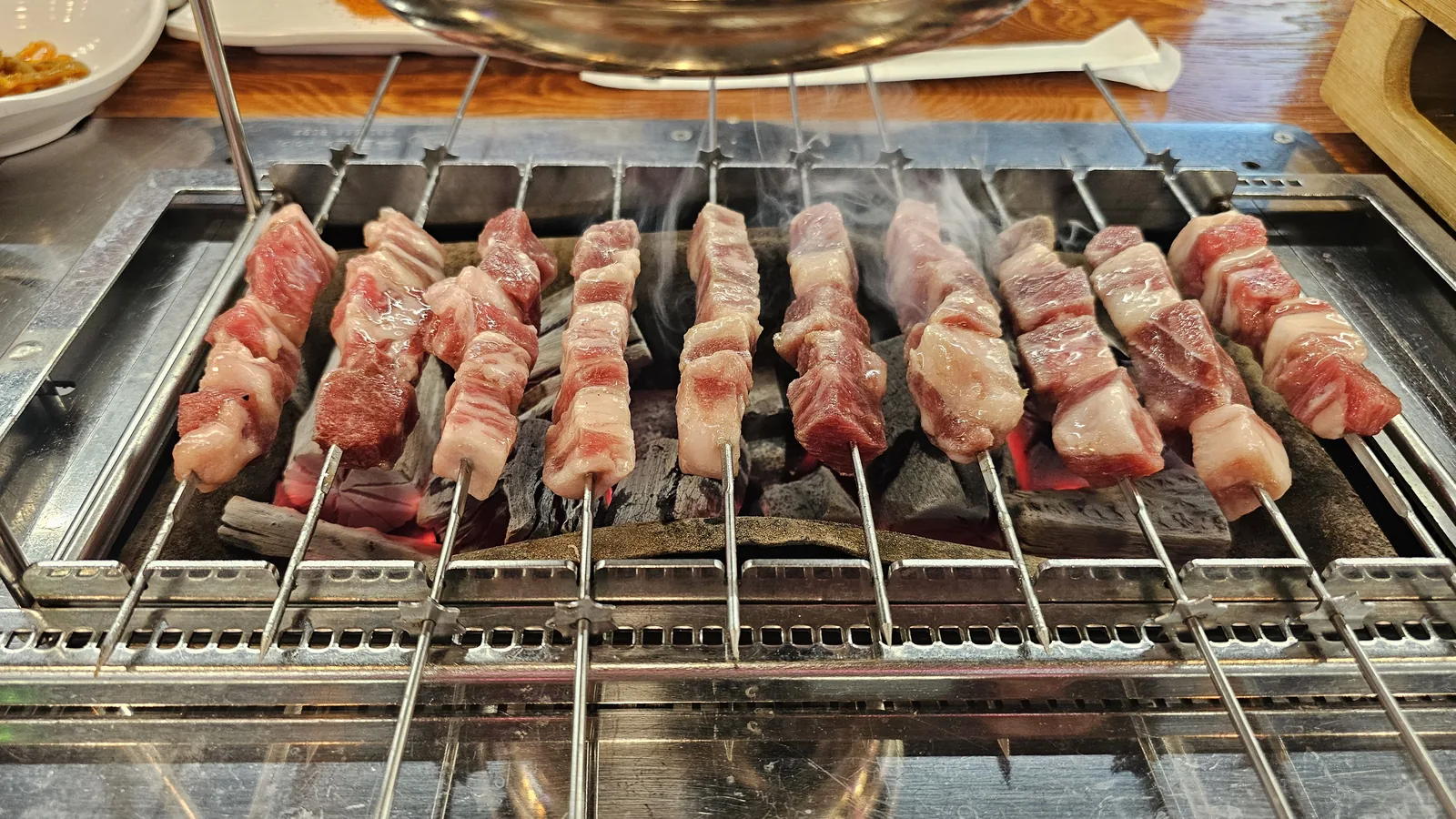 Lamb skewers sizzling on charcoal grill with smoke rising at Miyeon Yangkkochi Maratang