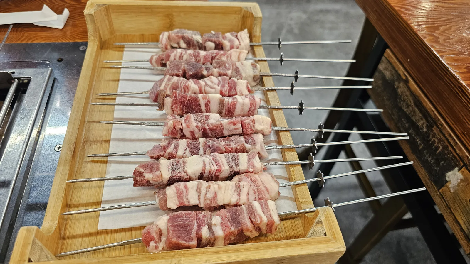 Raw lamb skewers on wooden tray before grilling, side view at Miyeon Yangkkochi