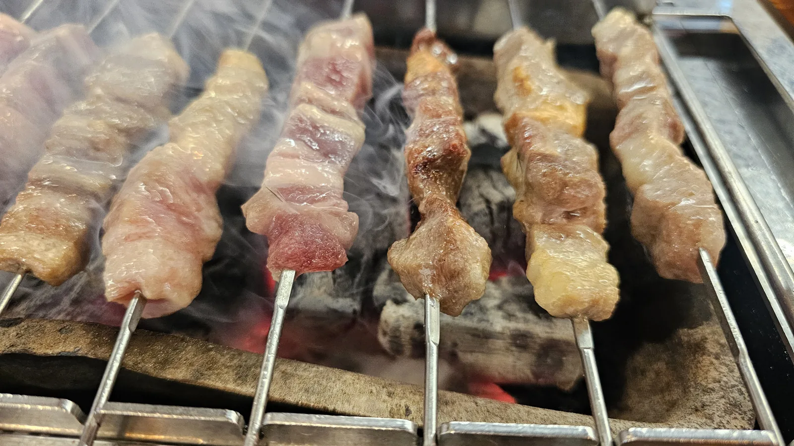 Lamb skewers half-cooked on charcoal grill turning golden brown at Miyeon