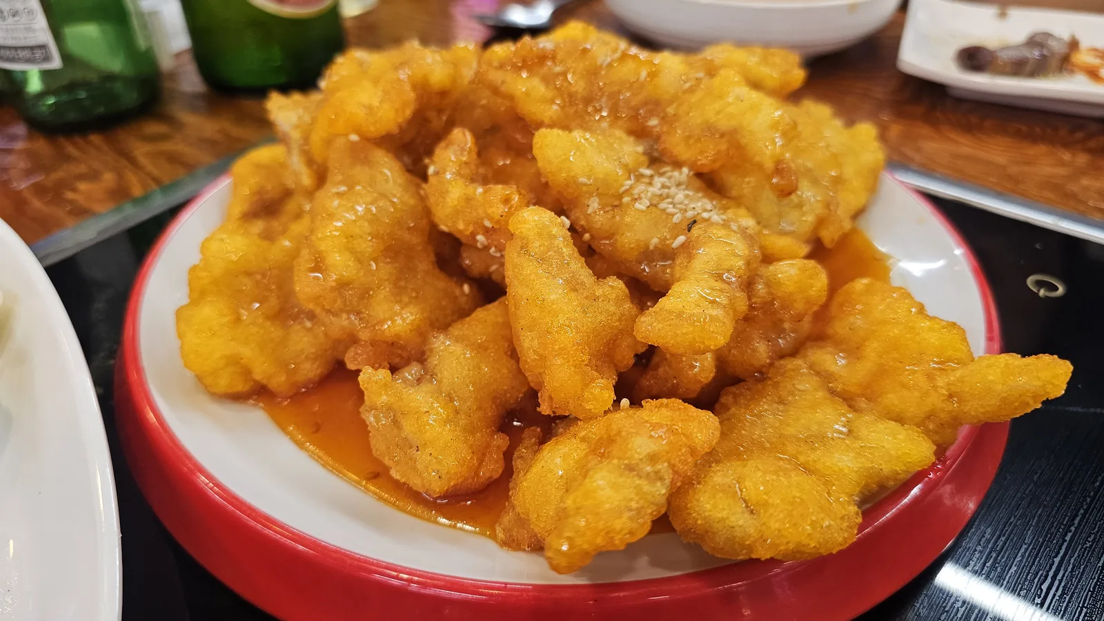 Tangsuyu sweet and sour pork on red-rimmed plate with dipping sauce and sesame seeds at Miyeon Cheongyang