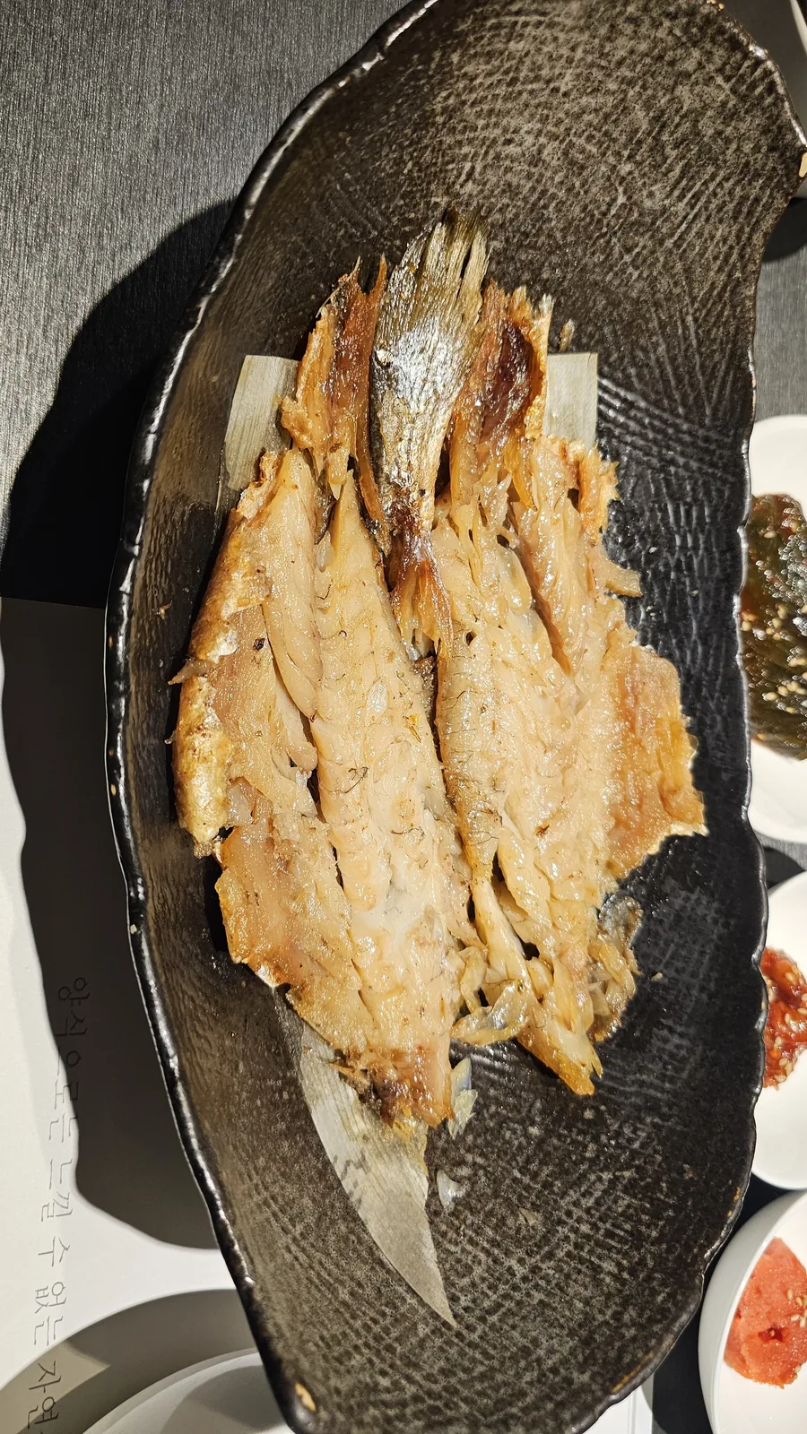 汝矣島ムッキの黒い陶器の皿に盛られた、竹の葉を添えたボリグルビの焼き魚