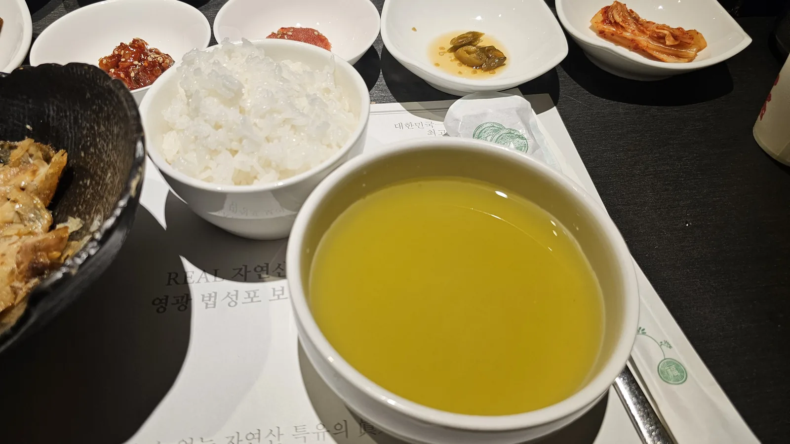 汝矣島ムッキでの食事中、テーブル全体の様子。ボリグルビの焼き魚、ご飯、緑茶水、各種バンチャンが並ぶ