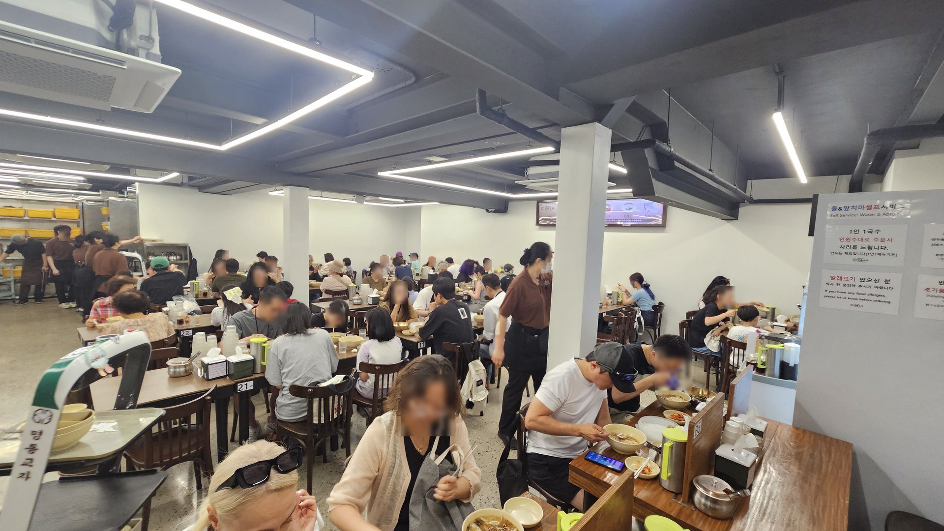 Crowded interior dining hall of Myeongdong Gyoja with bright fluorescent lighting and packed tables