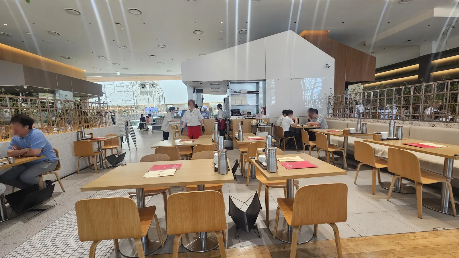 Bright interior of Sacheon Hwaga Yeouido with wooden tables, chairs, and red-uniformed staff in a wide open hall