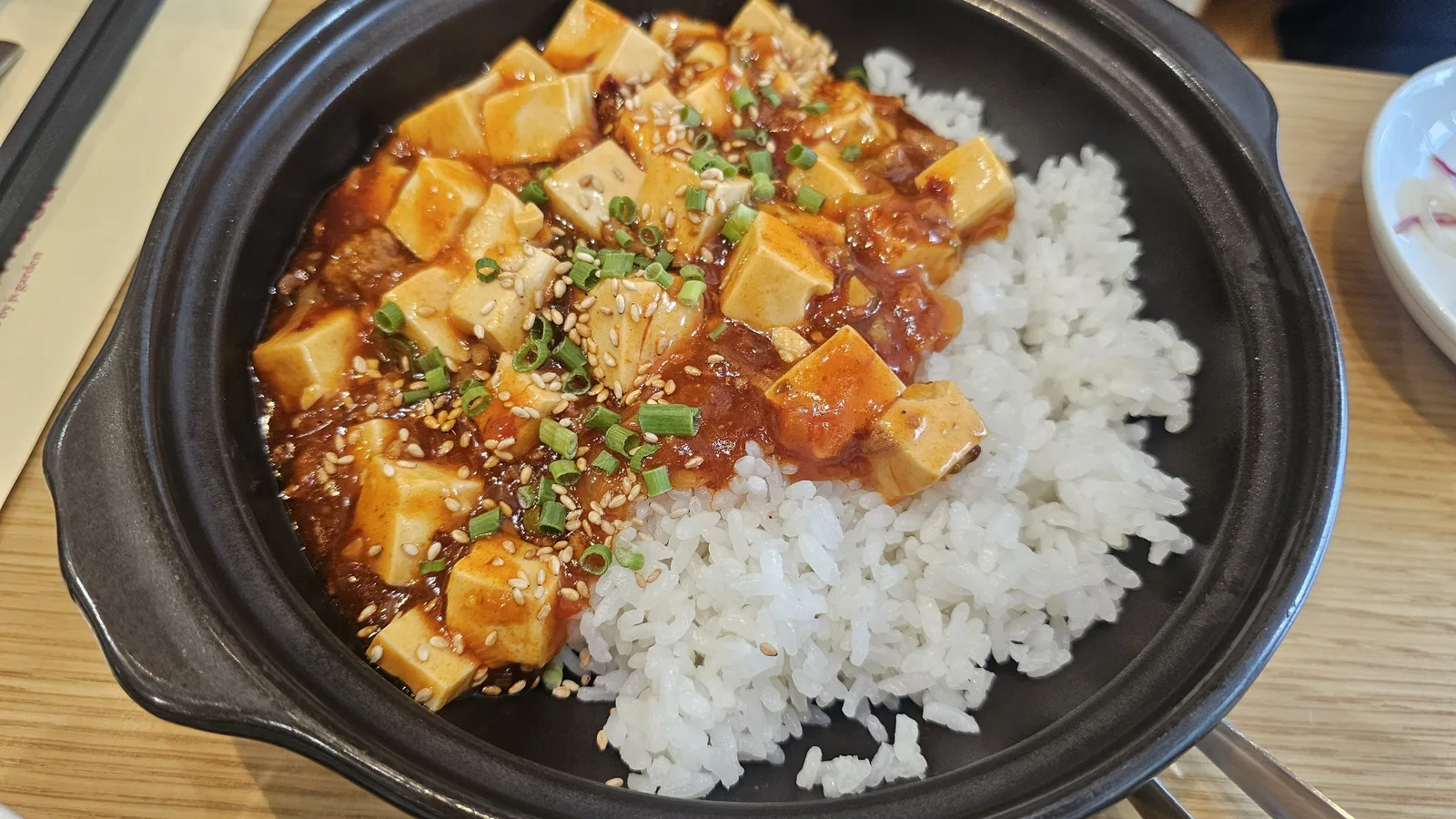 Mapo tofu rice served in black cast iron bowl with white rice, green onion and sesame at Sacheon Hwaga