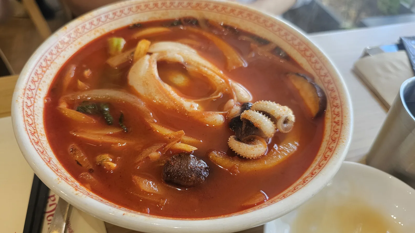 Sichuan-style seafood noodle soup (jjamppong) with thick noodles, squid and shiitake mushrooms in deep red spicy broth