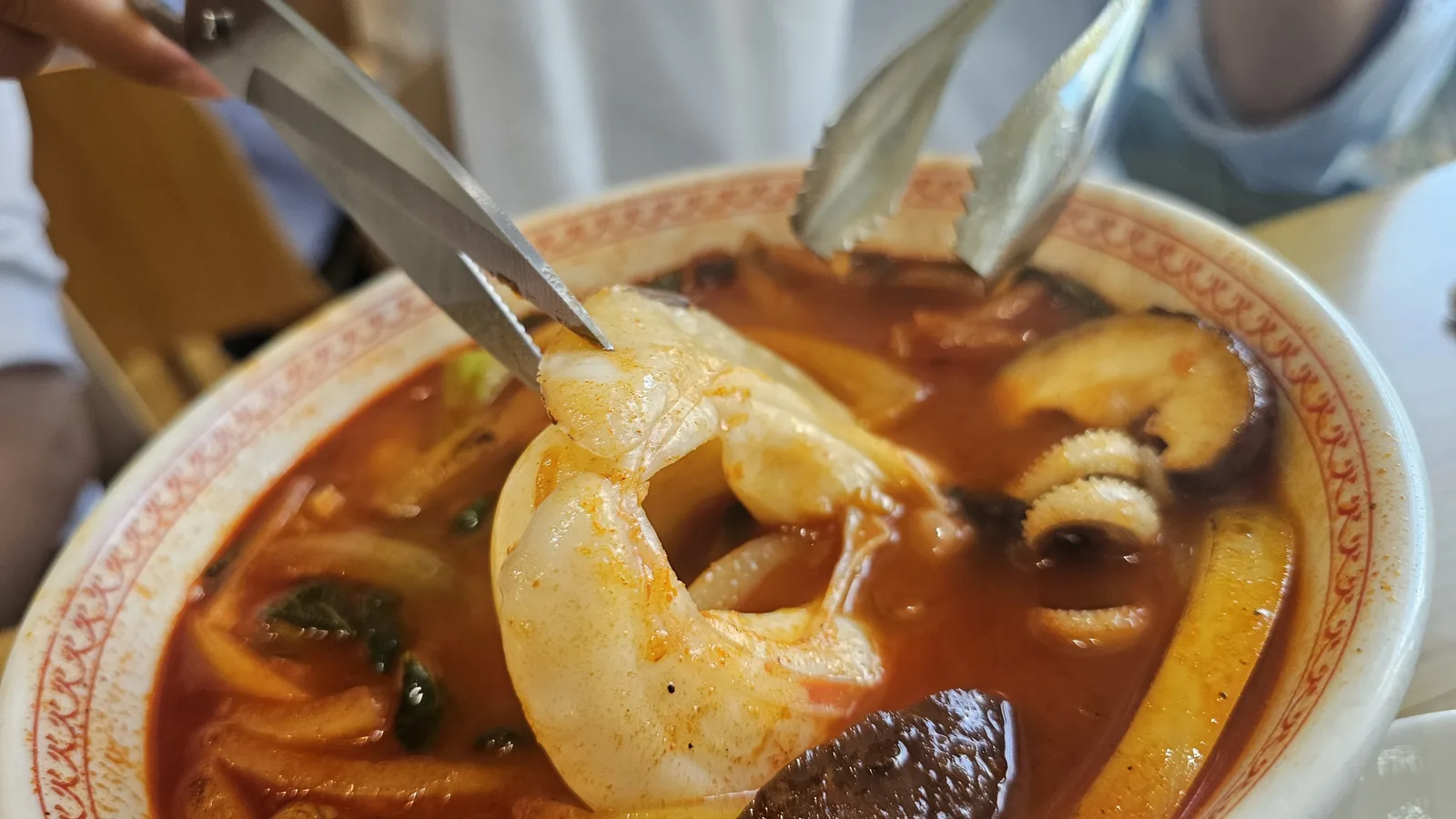 Close-up of Sichuan seafood noodle soup with large shrimp being cut by scissors at Sacheon Hwaga Yeouido