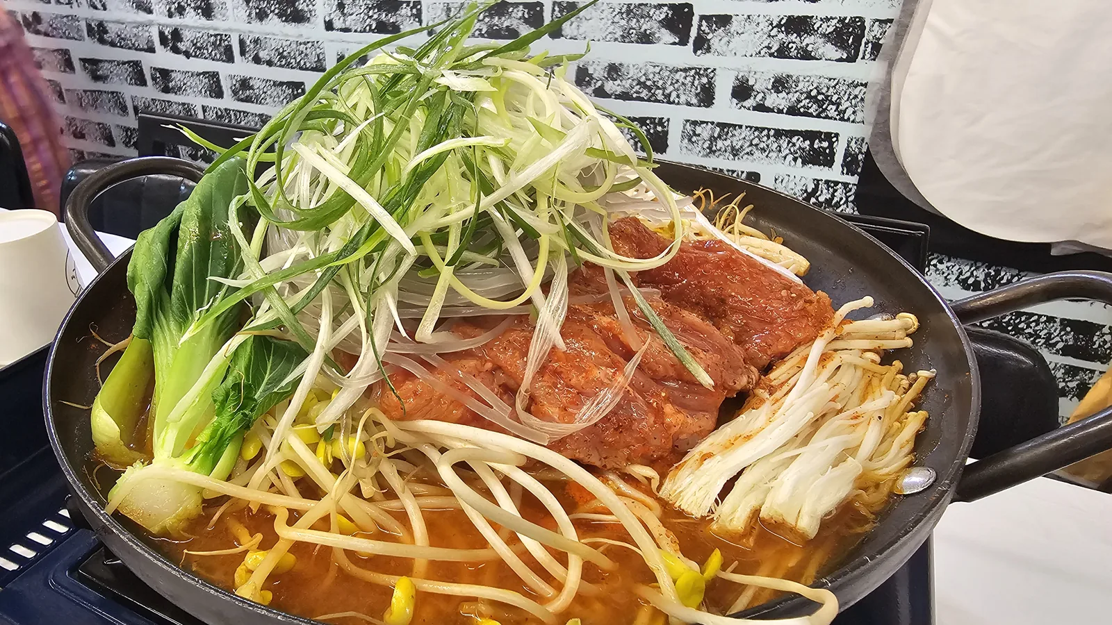 Sejong mulkalbi pork rib hot pot before cooking with sliced green onion, bean sprouts, and enoki mushrooms on tabletop burner