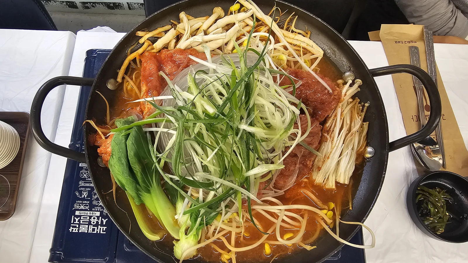 Overhead view of sejong mulkalbi pork rib pan with green onion strips and bok choy on portable burner