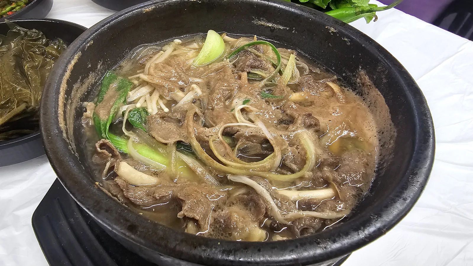 Dark stone pot ttukbaegi with rich galbi broth, glass noodles, mushrooms, and bok choy at Sejong Daewang Jeonju
