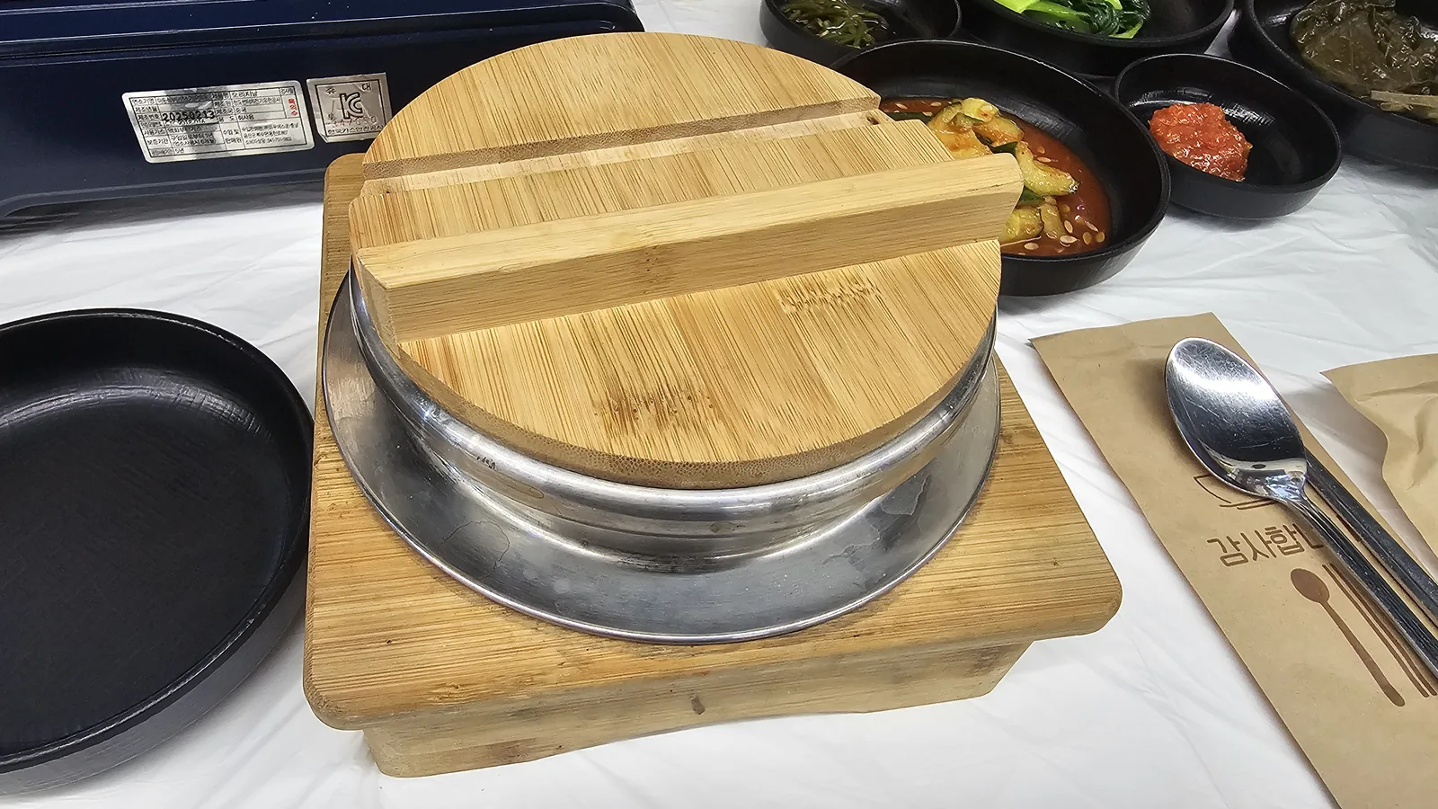Sotbap metal rice pot with bamboo lid on wooden board at Sejong Daewang Hangari