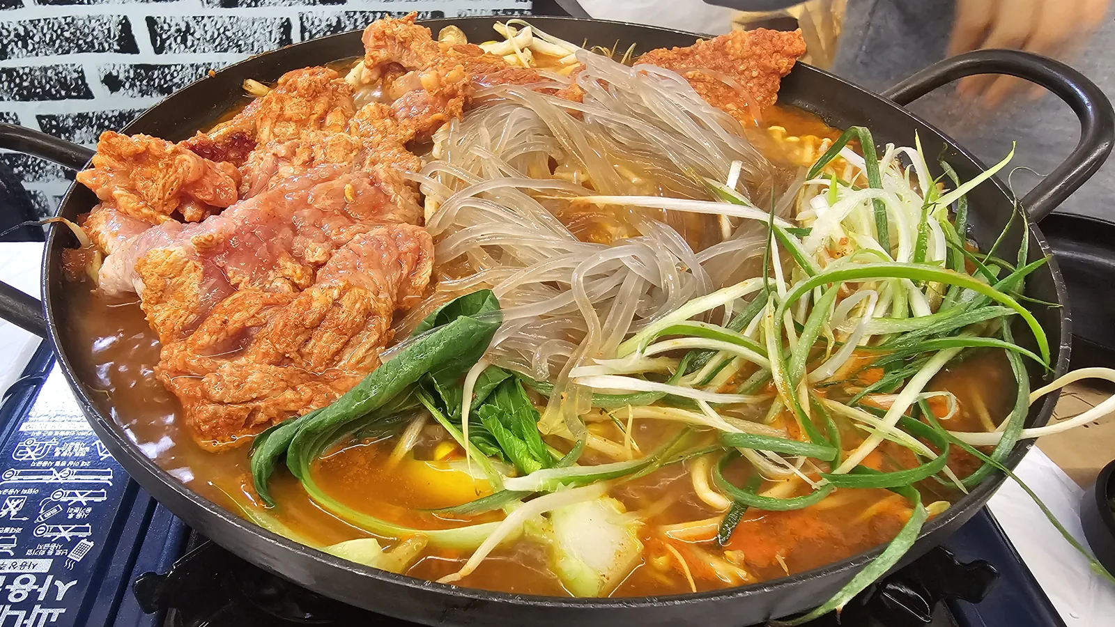 Spicy wang-galbi stew before cooking with rib meat, glass noodles, green onion, bean sprouts, and bok choy on tabletop burner
