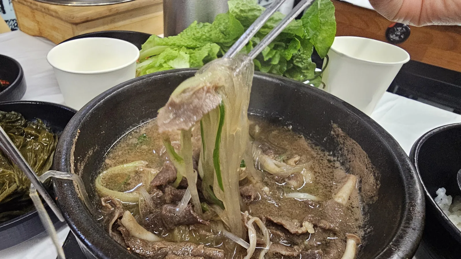 Dark stone pot galbi soup with chopsticks lifting glass noodles and rib meat at Sejong Daewang