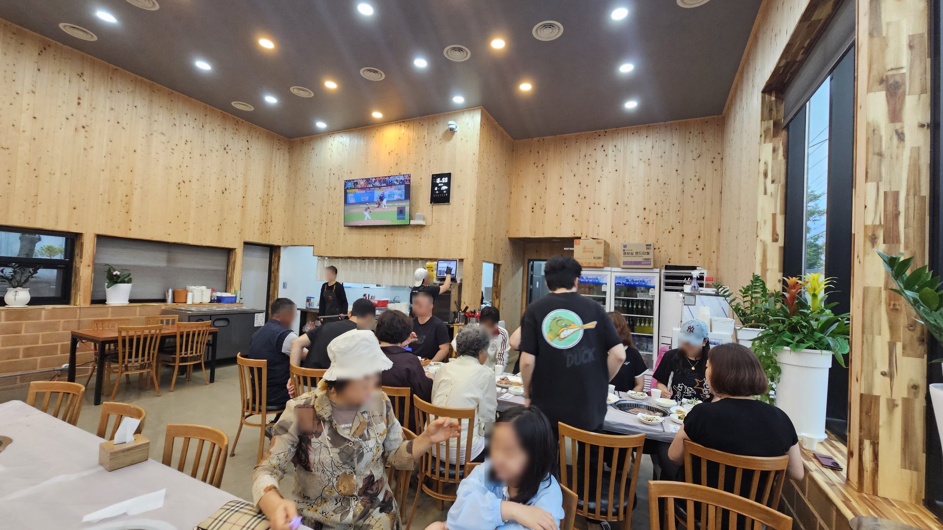 Wooden interior dining hall at Songnim Cheongyang with warm lighting, TV, and seated customers during evening service
