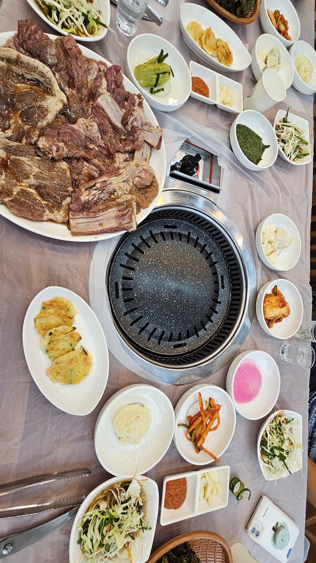 Full table setup at Songnim — center grill, marinated galbi, gamja-jeon potato pancake, green onion salad, and side dishes
