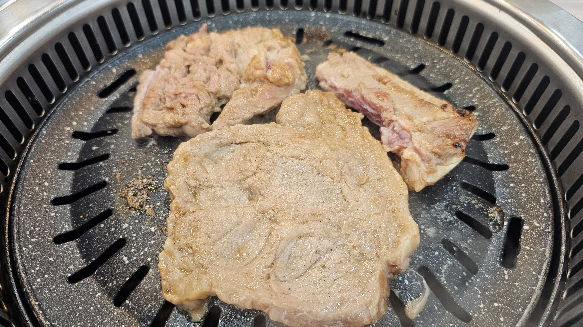 Three pieces of marinated pork ribs cooking mid-grill on the BBQ at Songnim