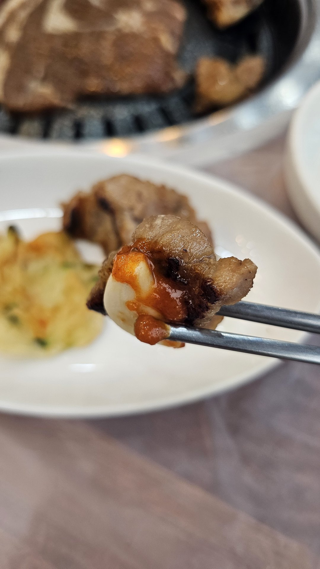 Chopsticks lifting a piece of grilled galbi dipped in sauce at Songnim, gamja-jeon visible in background