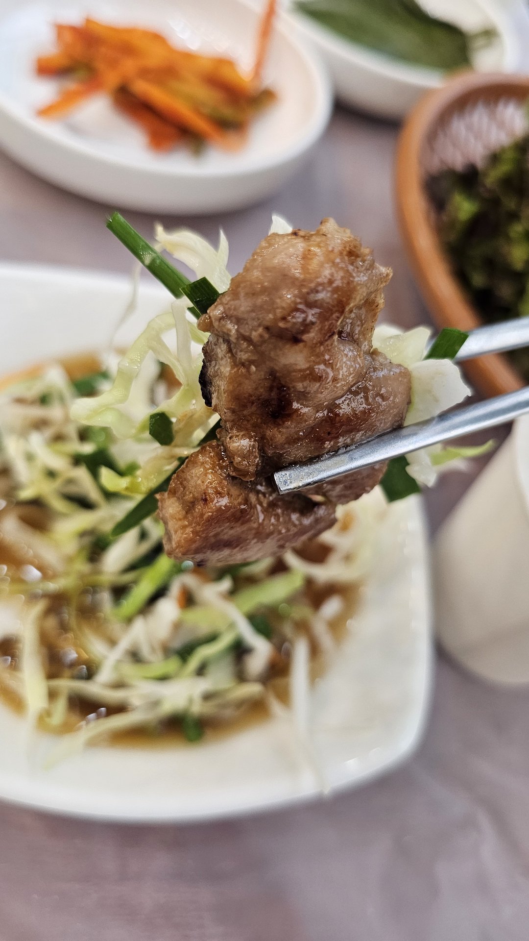 Close-up of chopsticks holding a piece of grilled galbi over green onion salad at Songnim