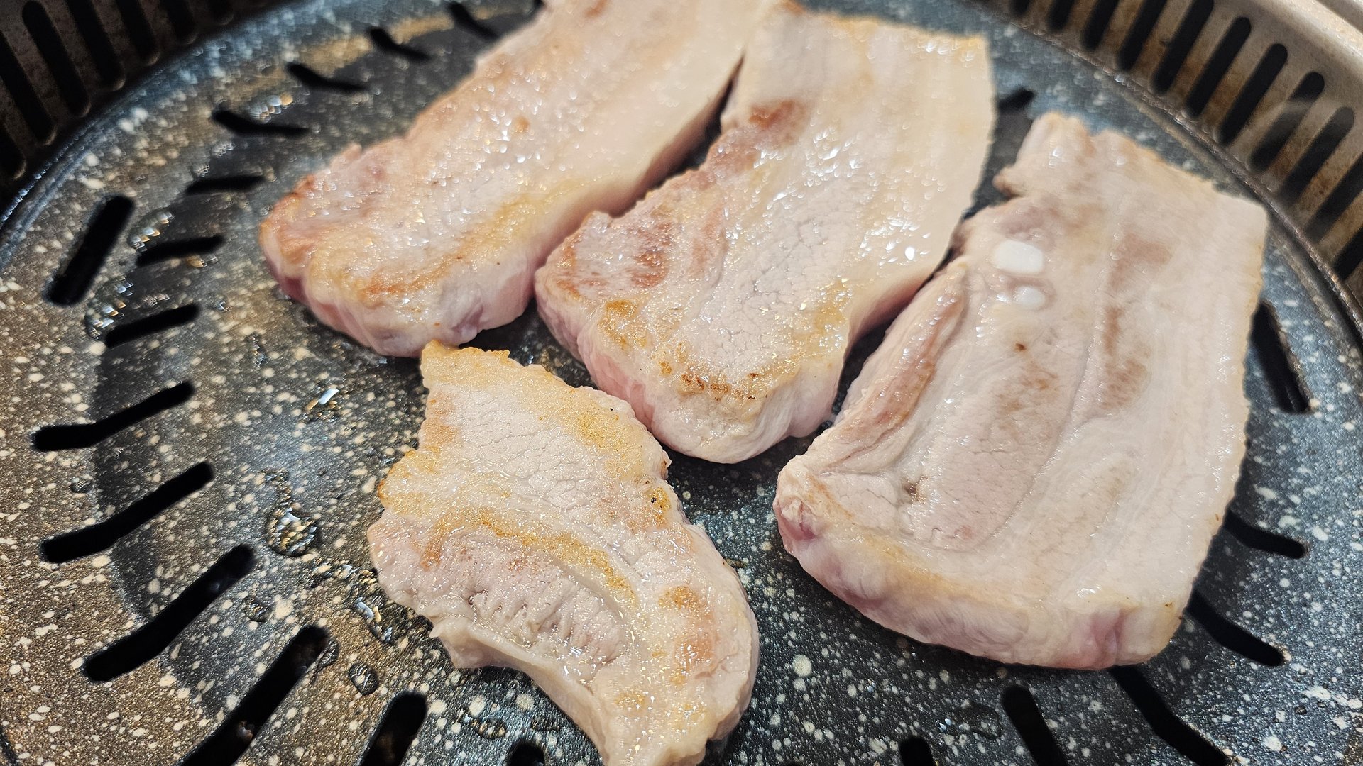 Four thick slices of pork belly just placed on the tabletop BBQ grill at Songnim