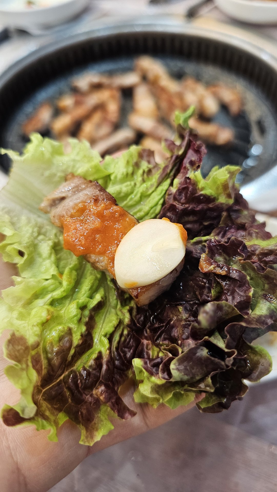 Hand holding a ssam wrap with pork belly, garlic, and ssamjang in a lettuce leaf at Songnim