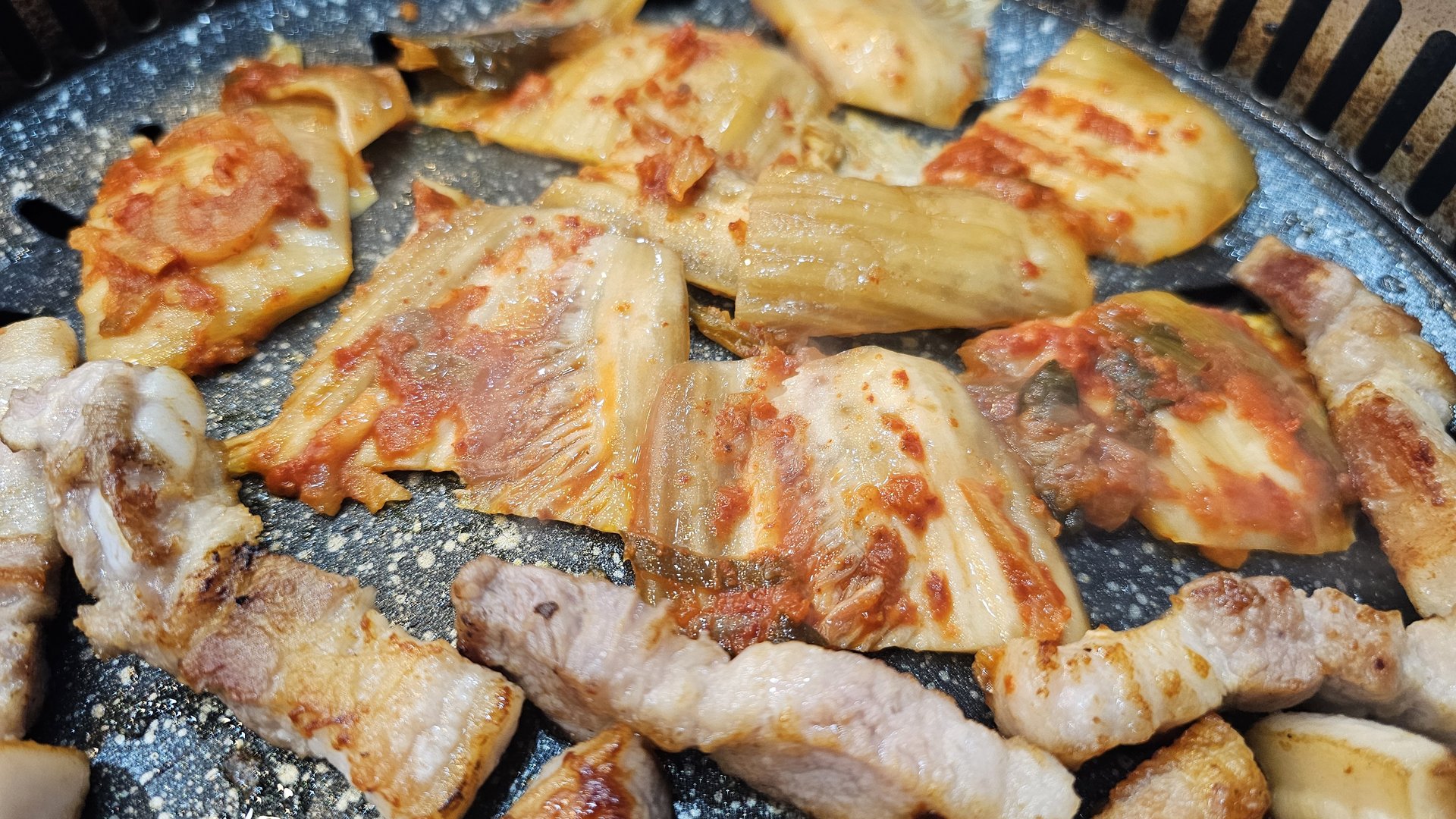 Pork belly and kimchi grilling together on the BBQ at Songnim Cheongyang, kimchi caramelized