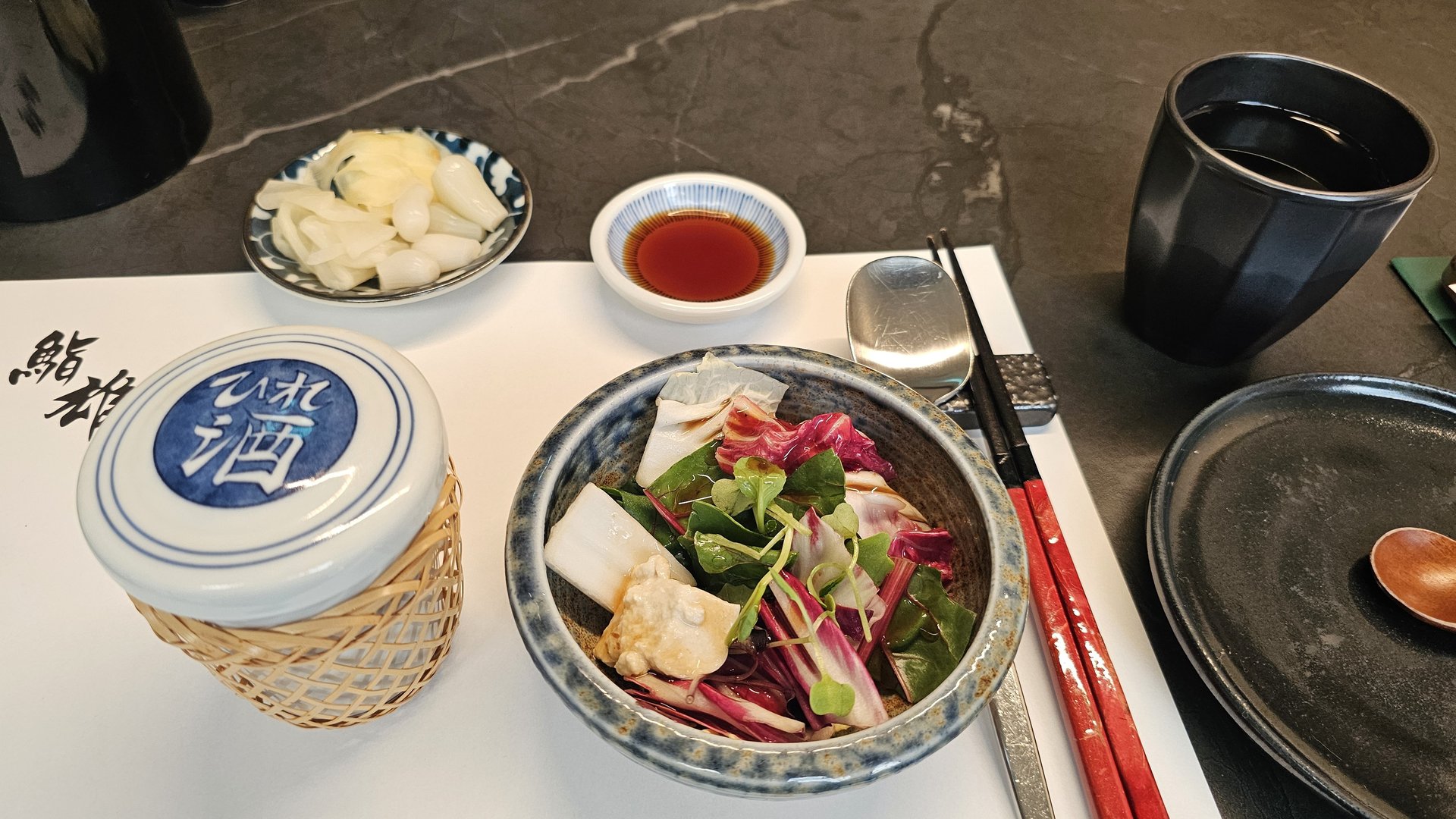 Starter salad with seafood and vegetables at Sushi Yu, served alongside pickled ginger, soy sauce, and green tea on a logo table mat