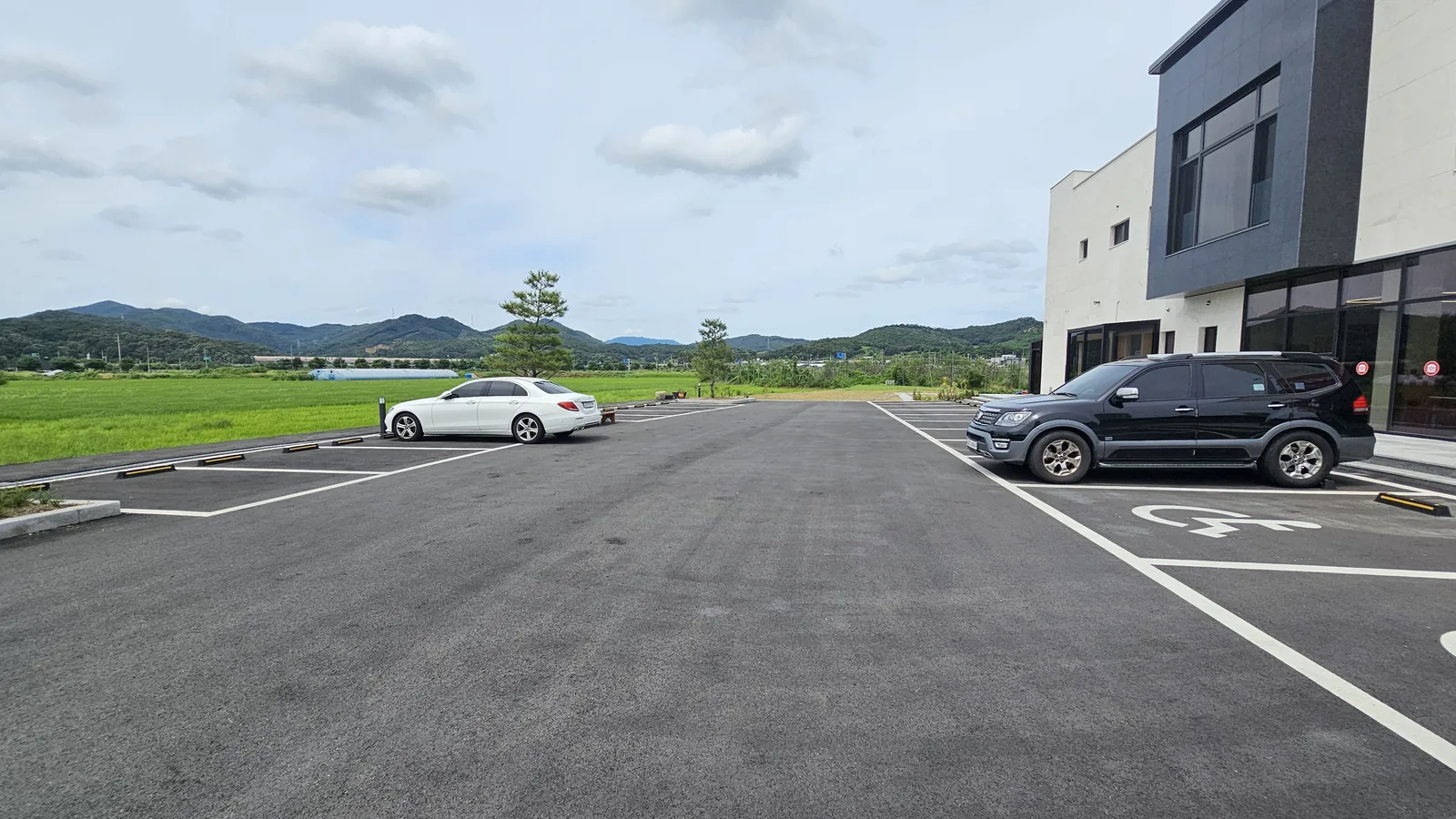 ワット・ザ・バーガー청양店の隣にある広々とした駐車場。背景には田んぼと山並みが広がっている
