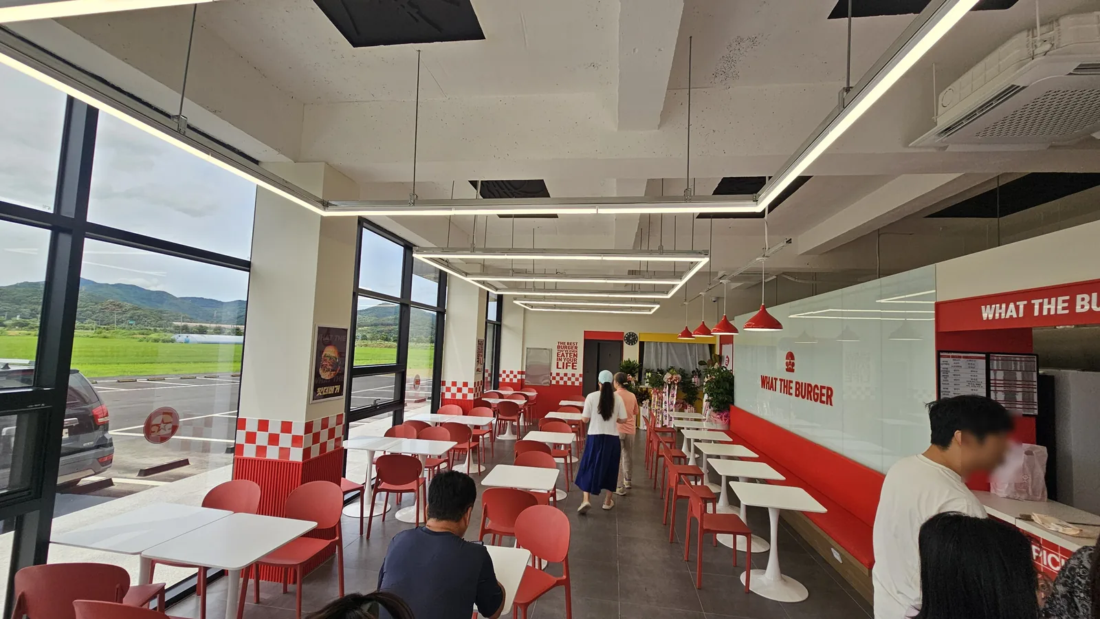 ランチタイムに客が並ぶ、ワット・ザ・バーガー청양店の明るい赤と白の店内とボックスシート