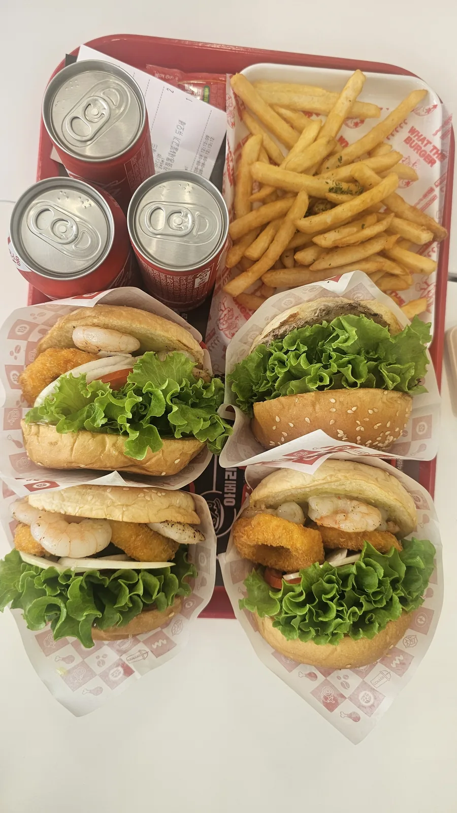 ワット・ザ・バーガー청양店のトレイ全体。バーガー4つ、フライドポテト、コカ・コーラ缶3本