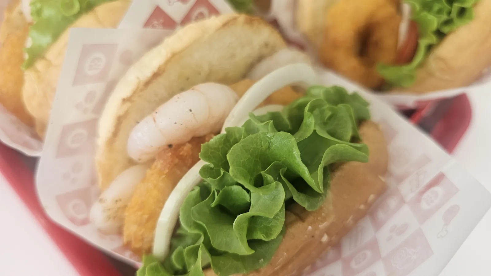 직화（ジクファ）통새우（トンセウ）丸ごとエビバーガーの断面クローズアップ。エビ、揚げパティ、レタスの層が見える