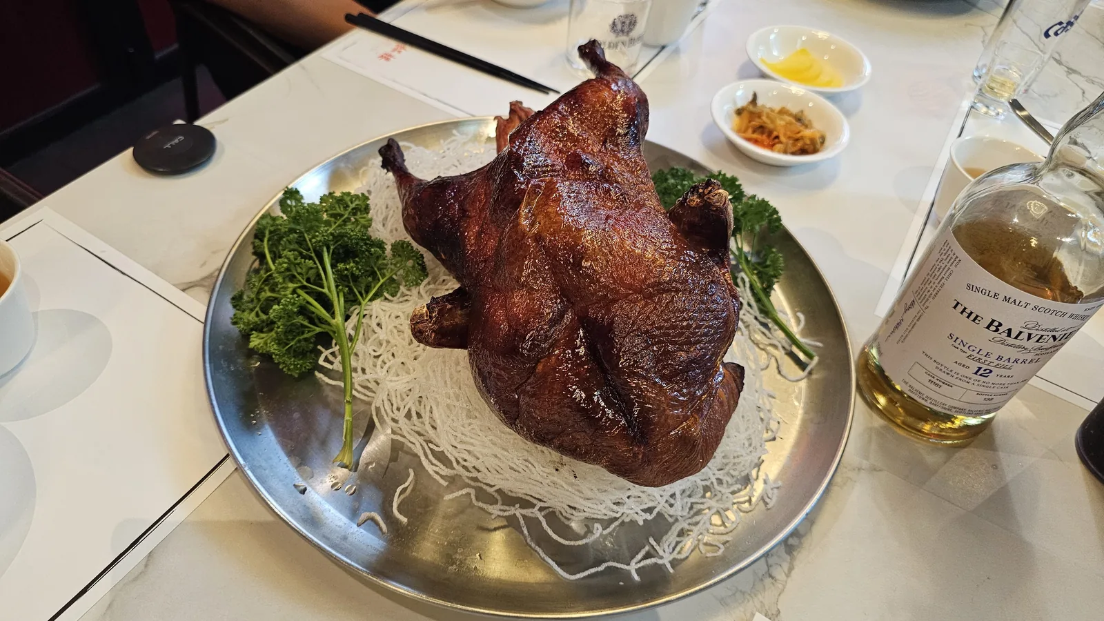 Whole Peking duck on silver platter with chopsticks reaching in at Xin Hong Lou