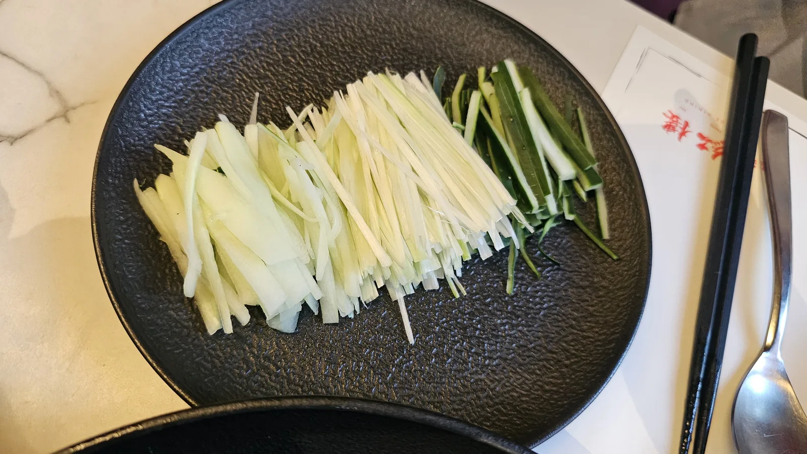 Julienned scallions and cucumber on black plate for Peking duck wrapping at Xin Hong Lou
