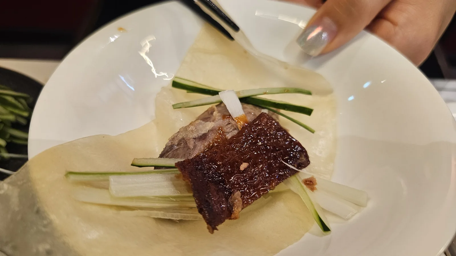 Peking duck wrap assembled with duck slices cucumber and scallions in thin crepe close-up at Xin Hong Lou